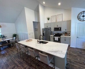 A modern kitchen with a large island, stainless steel appliances, and a dining area with a bench. - 1/2 Acre Fenced In Private Oasis (Wilmington)