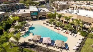 Ett semesterhotell med en central pool omgiven av solstolar och palmer.