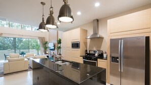 Une cuisine moderne dotée d’un îlot central, d’appareils électroménagers en acier inoxydable et de luminaires suspendus.