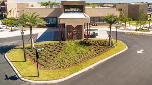 A modern building with a central entrance, surrounded by landscaped gardens and palm trees. - Gorgeous 3BDHome/Near Disney/No Fees/Free Parking/Wi-Fi/BBQ Grill/Shared Pool (Kissimmee)