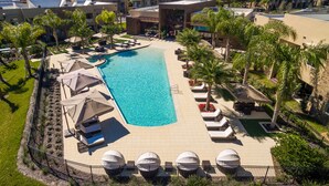 Ein Luftbild eines Resorts mit Schwimmbad, Liegestühlen und Palmen.