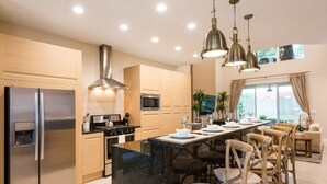A modern kitchen with stainless steel appliances, a central island with bar stools, wooden cabinets, and pendant lighting. - Near Disney/Gorgeous home/ Parking/ BBQ Shared Heated Pool (Kissimmee)