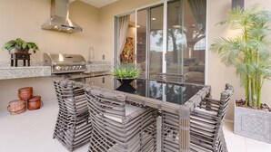 Una cocina moderna con extractor de acero inoxidable, parrilla empotrada y una mesa de comedor de vidrio con sillas de mimbre.