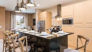 Una cocina moderna con una isla central, armarios de madera, electrodomésticos de acero inoxidable y un comedor con cuatro sillas y una mesa.