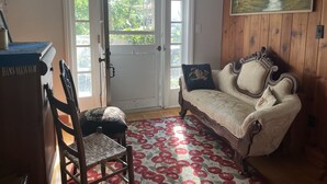 Una habitación con puerta de madera, un sofá antiguo y un tapete con estampado floral, además de un cuadro en la pared.