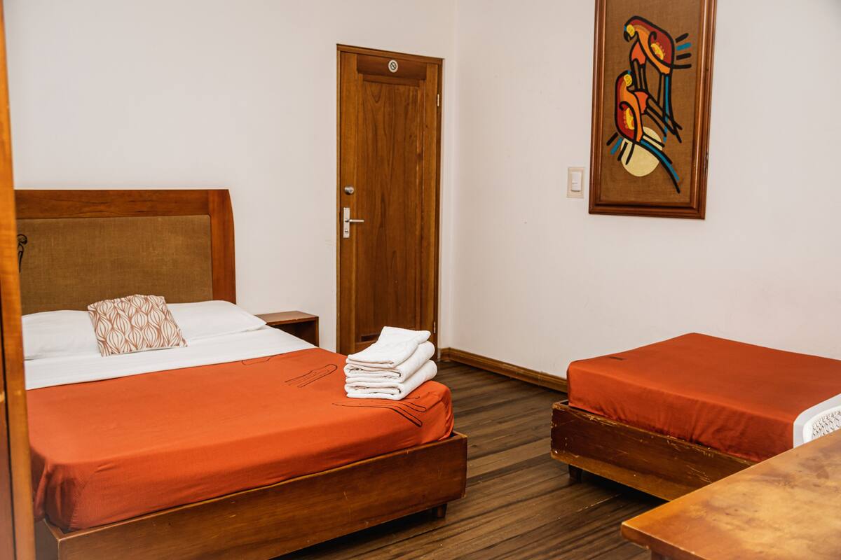 Ein Hotelzimmer mit einem hölzernen Bett, einem Nachttisch aus Holz, einer Tür und einem Bild an der Wand.
