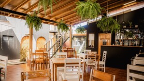 A restaurant with wooden tables and chairs, hanging plants, and a bar area with shelves of bottles and glasses. - Luz De Luna Hotel Barrio Escalante (San José)