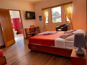 Ein Hotelzimmer mit Bett, Schreibtisch, Stuhl, Fernseher und einem Fenster mit Vorhängen.