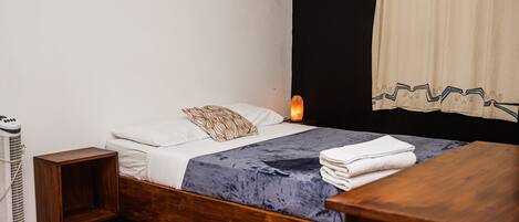 A bedroom with a wooden bed, white bedding, a bedside table, a heater, and a window with curtains.
