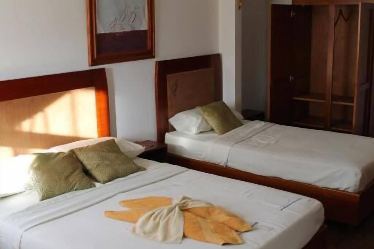 Zwei Einzelbetten mit Holz Kopfteilen und weißer Bettwäsche, ein gerahmtes Bild an der Wand und ein Holzschrank im Hintergrund.