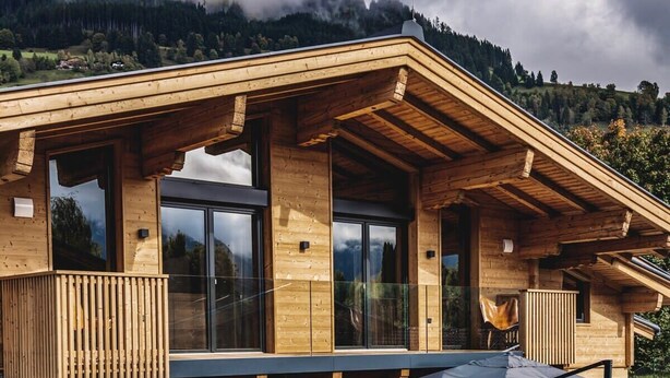 Una cabaña de madera con ventanas amplias, un balcón y vistas a un paisaje montañoso.