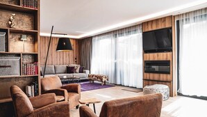 Una sala de estar moderna con un sofá, sillones, una mesa de centro, una estantería, un televisor de pantalla plana y una chimenea.