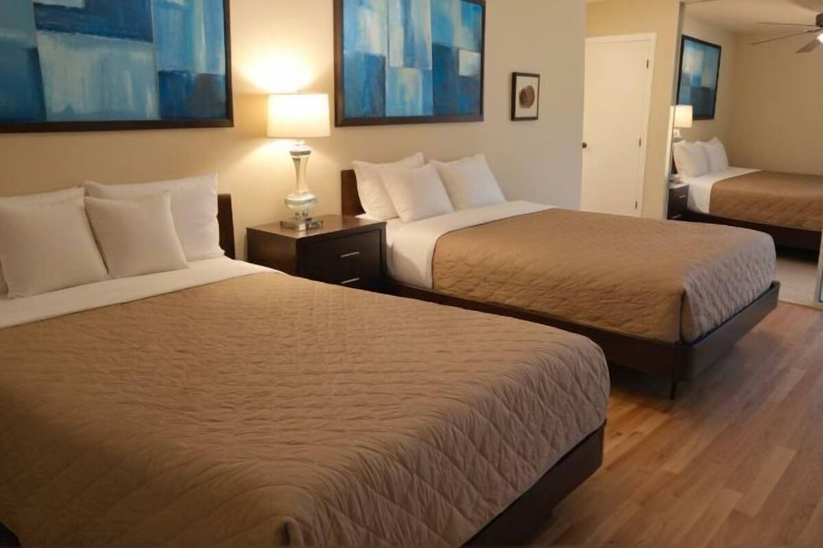 A hotel room with two beds, a nightstand, a lamp, and abstract art on the walls.