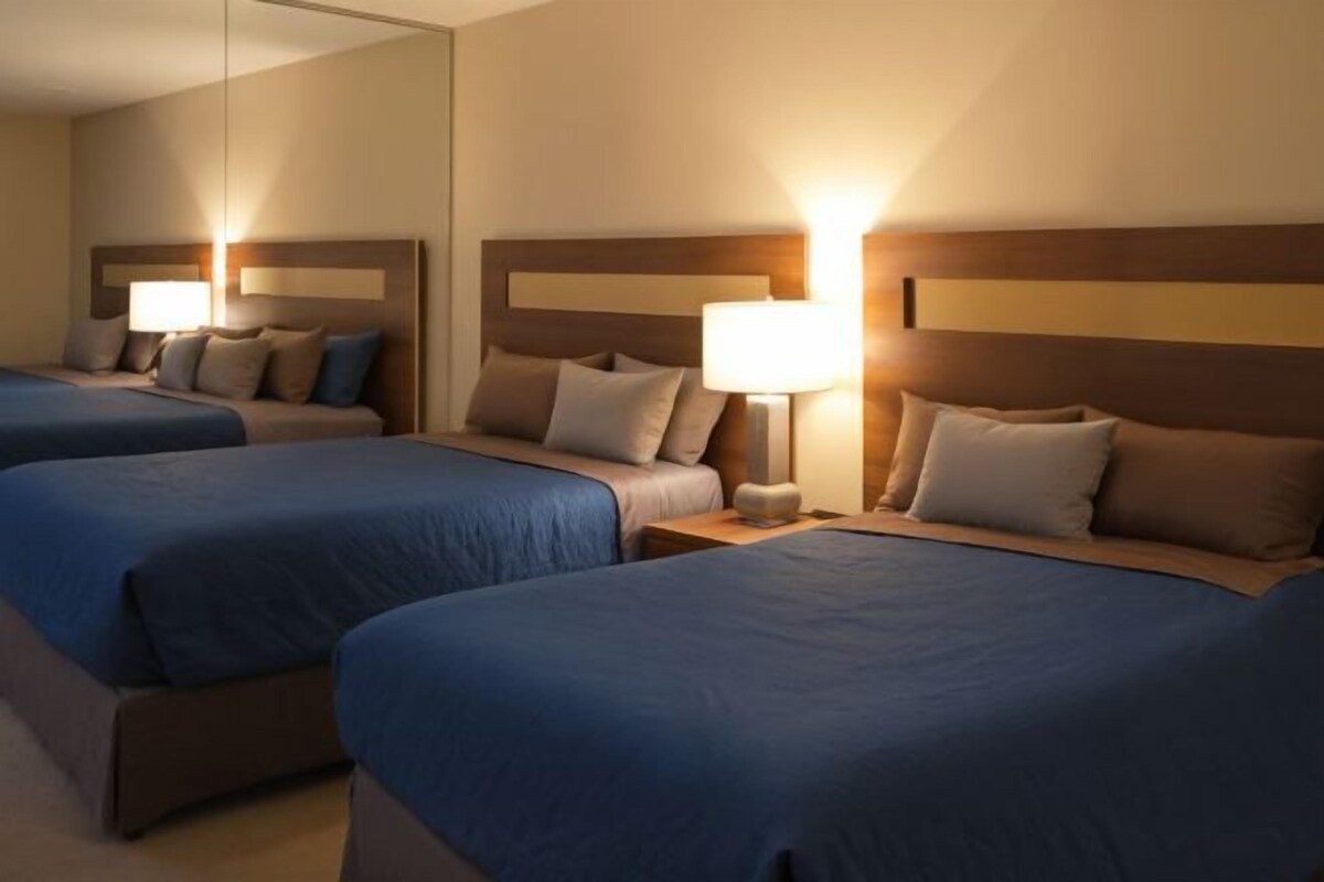 Quarto de hotel com duas camas, cada uma com cabeceira, mesas de cabeceira e luminárias.