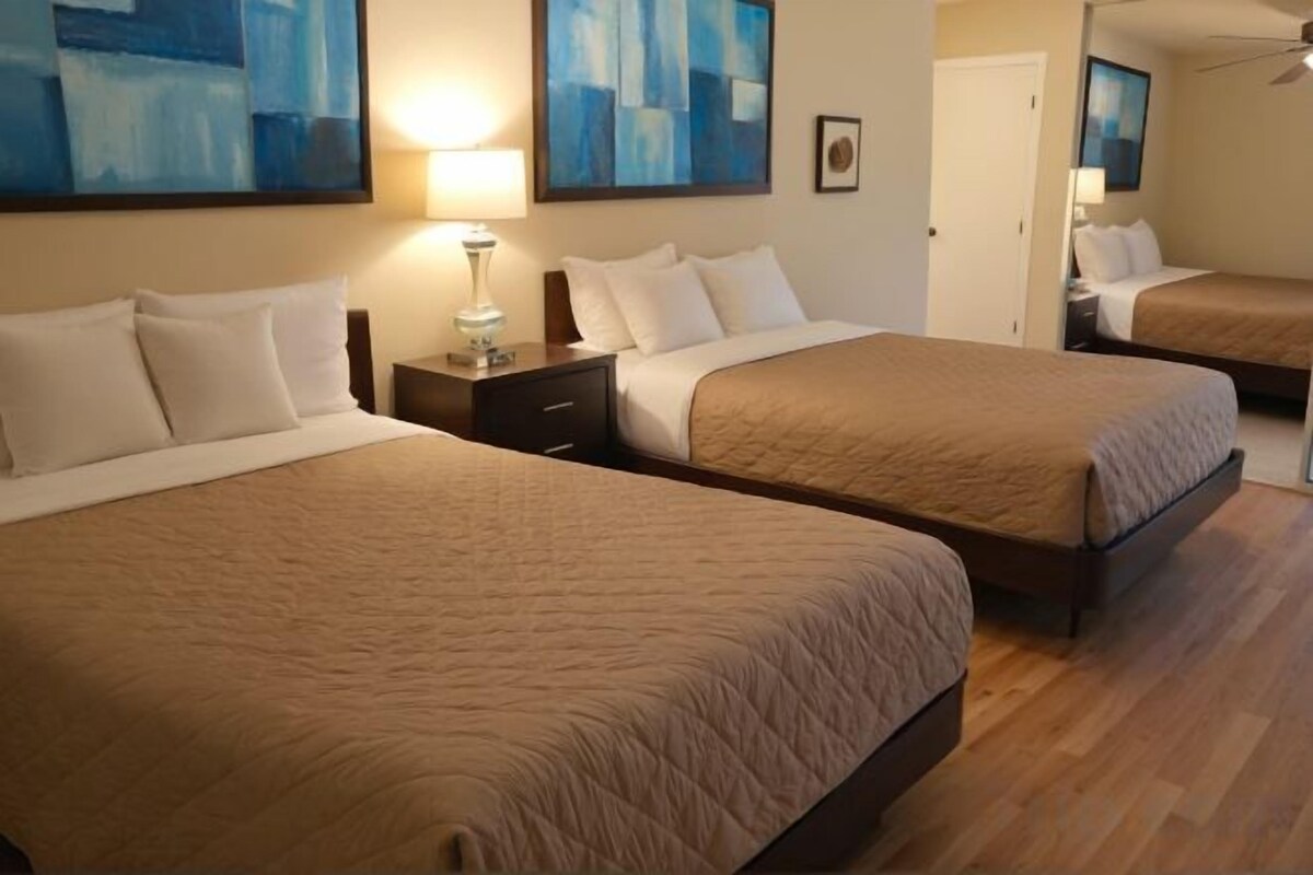 Two queen beds with a wooden floor, a nightstand with a lamp, and artwork on the walls.