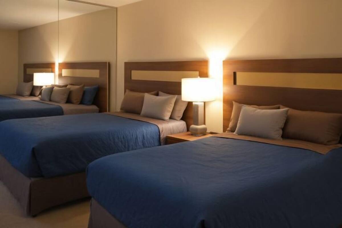 A hotel room with two beds, each with a headboard, bedside tables, and lamps.