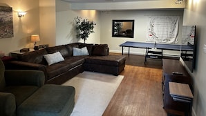Ein Wohnzimmer mit Ecksofa, einem kleinen Tisch, einem Tischtennisplatten und einem großen Spiegel.