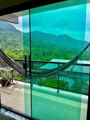 A room with a large glass window offering a view of a lush green landscape and mountains. - Pousada Ohana Paraty (Paraty)