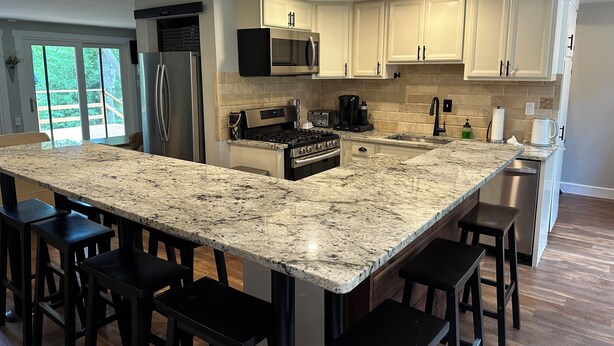 A modern kitchen with a large granite island, stainless steel appliances, and white cabinetry. - Riverfront Cabin – Summertime Escape in the Shenandoah Valley (Shenandoah)