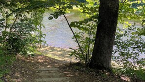 A wooden pathway leading to a body of water, surrounded by trees and foliage. - Riverfront Cabin – Summertime Escape in the Shenandoah Valley (Shenandoah)