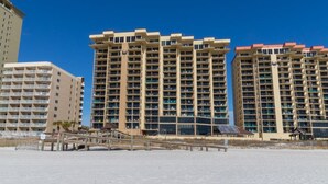 A beachfront hotel with multiple high-rise buildings, a sandy beach in the foreground, and a clear blue sky. - Phoenix I 1085 (Orange Beach)
