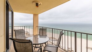 A balcony with a round table and chairs, overlooking a beach with a railing. - Phoenix I 1085 (Orange Beach)