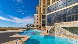 A swimming pool area with a stone wall and a building with large windows in the background. - Phoenix I 1085 (Orange Beach)