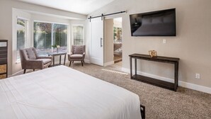A bedroom with a bed, two chairs, a small table, a TV, and a sliding door leading to a balcony. - Modern and Bright Resort Style Home w/Heated Pool (Las Vegas)