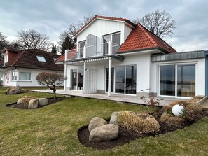 Une maison moderne à deux étages, dotée d’un balcon, de grandes fenêtres et d’une pelouse bien entretenue.