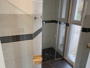 Un espace douche doté d’une porte en verre, de murs carrelés et d’une petite fenêtre.