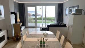 Ein moderner Essbereich mit Tisch für zwei, eine Küche mit Herd und Blick auf eine grüne Landschaft durch große Schiebetüren.
