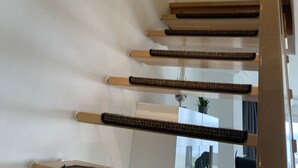 Eine Treppe mit Holzwegen und Geländer, die zu einer Zwischenebene mit einer weißen Wand und gerahmten Bildern führt.