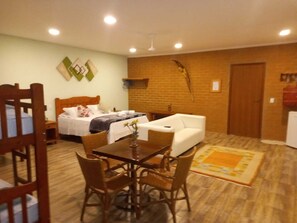 Um quarto acolhedor com uma cama, um sofá branco, uma mesa de jantar com cadeiras e uma pequena cozinha.