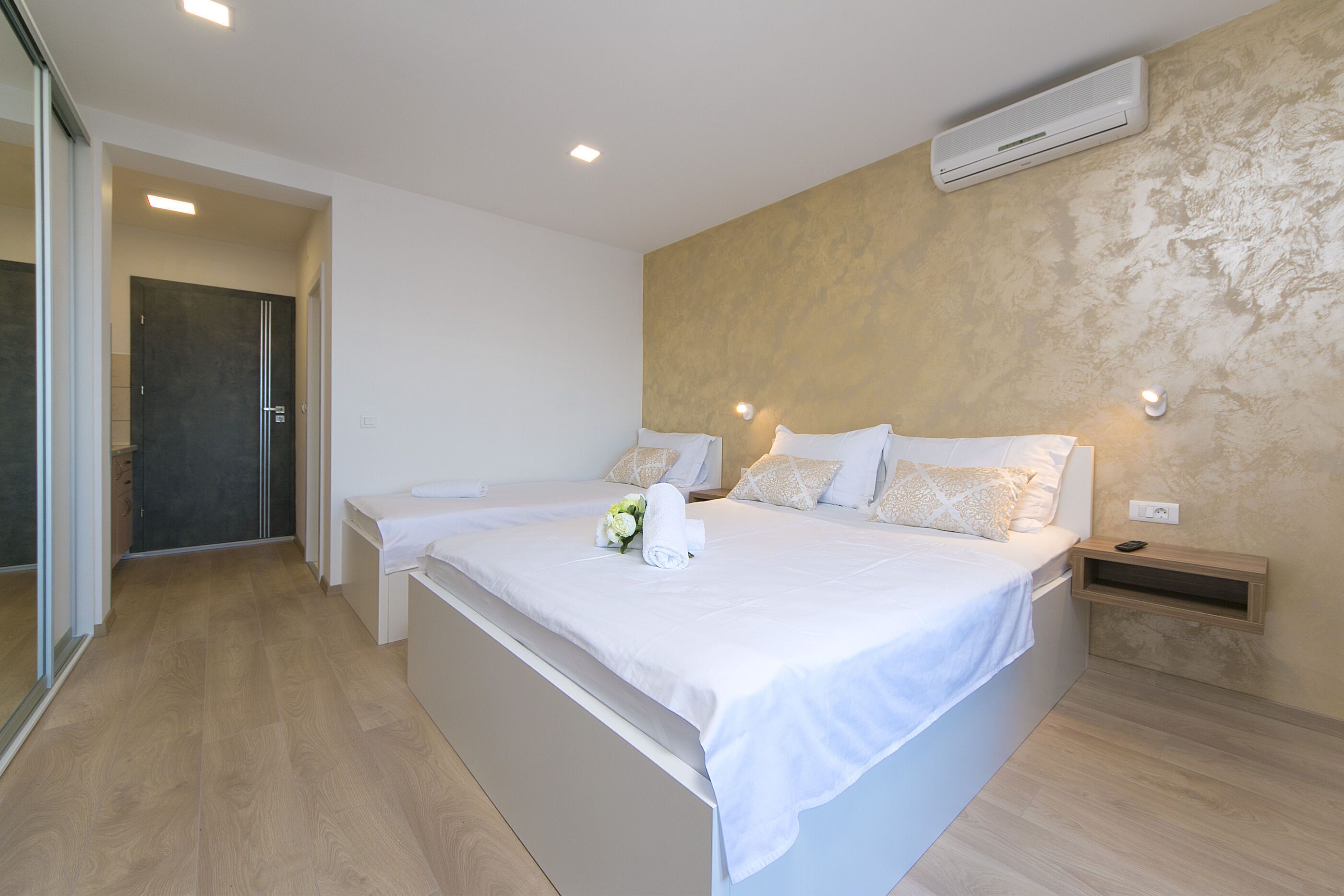 A modern bedroom with two beds, a wooden floor, and an air conditioning unit on the wall.