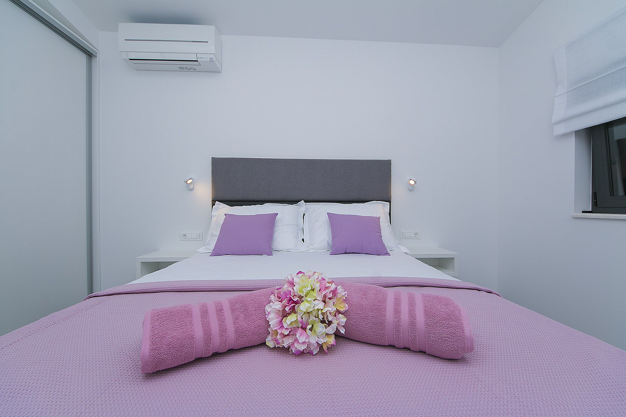 A modern bedroom with a bed, pillows, a headboard, and a wall-mounted air conditioner.