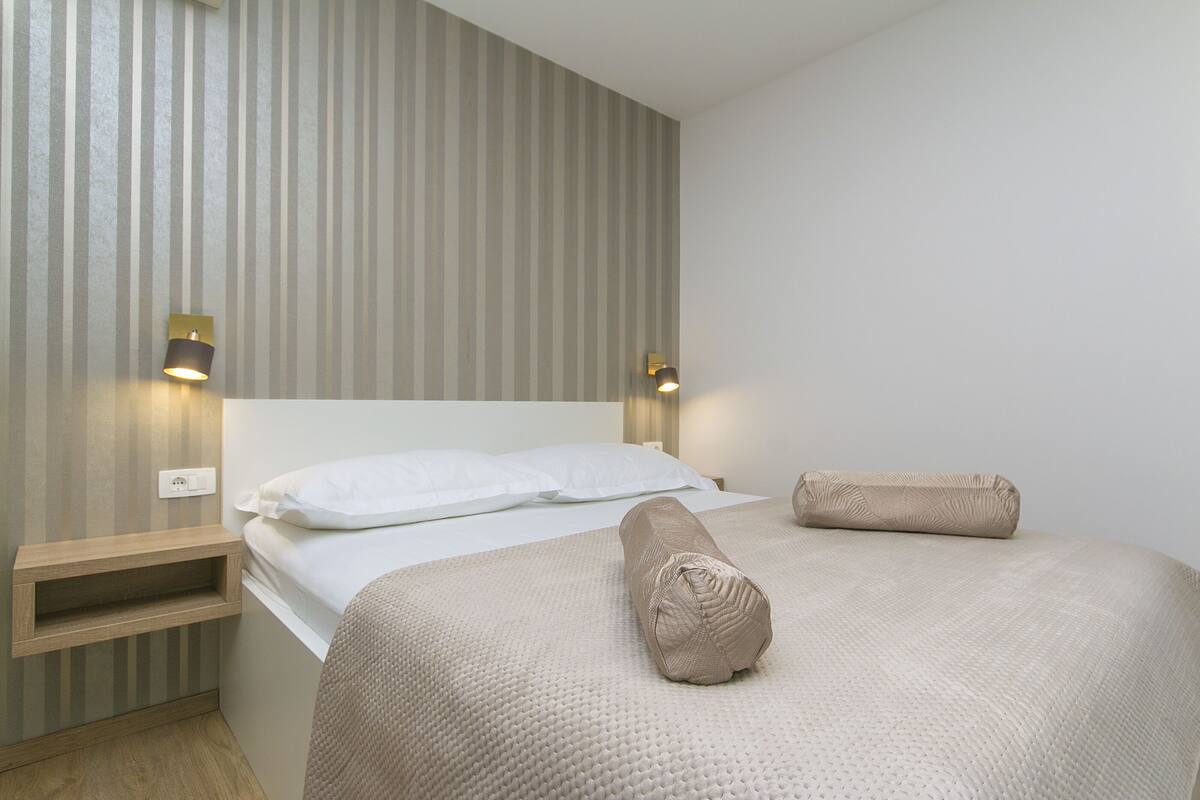 Un lit bien fait, recouvert d’une couverture à motifs, avec deux lampes de chevet et une table de nuit en bois.