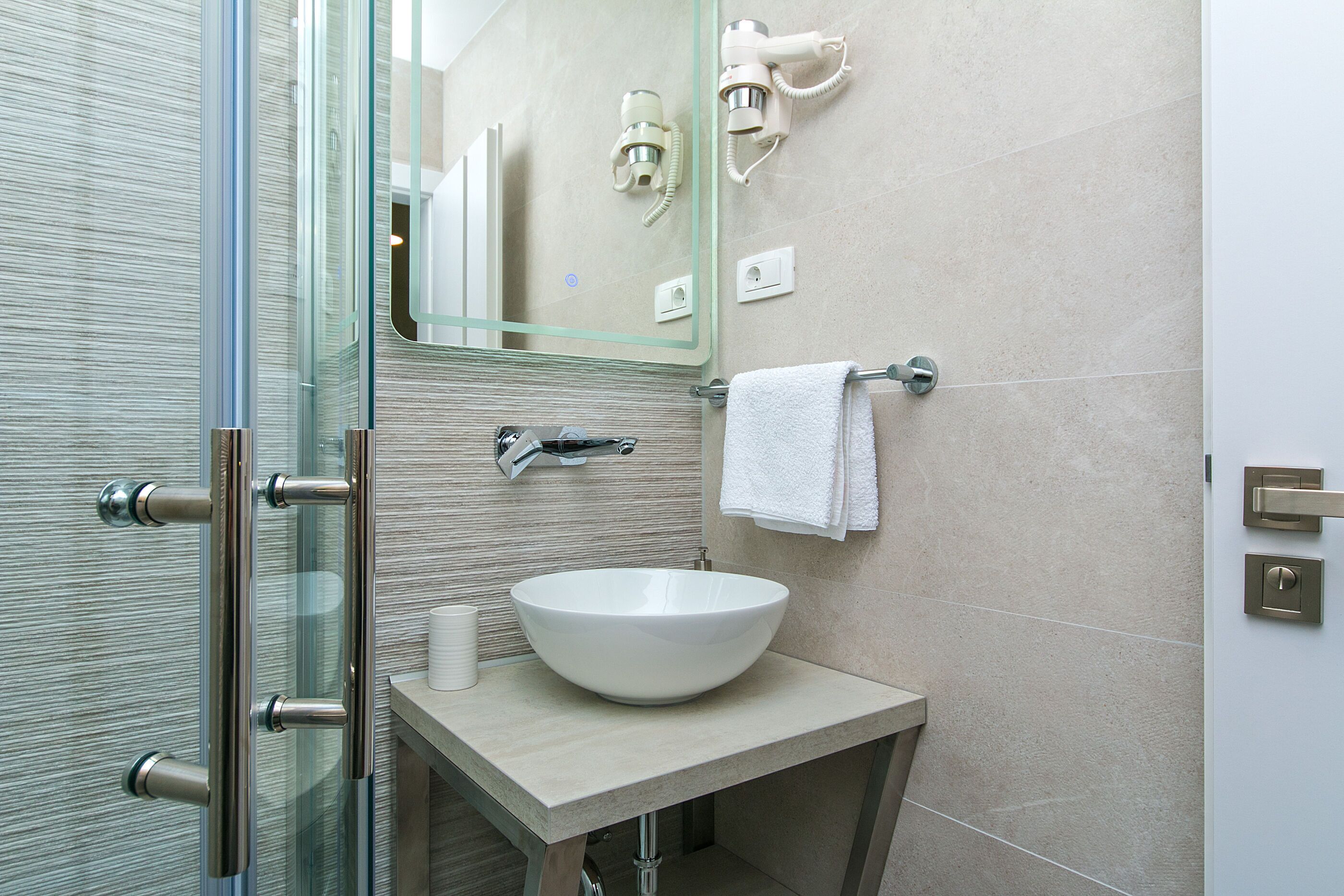 A modern bathroom with a glass shower enclosure, a white sink, and a towel rack.