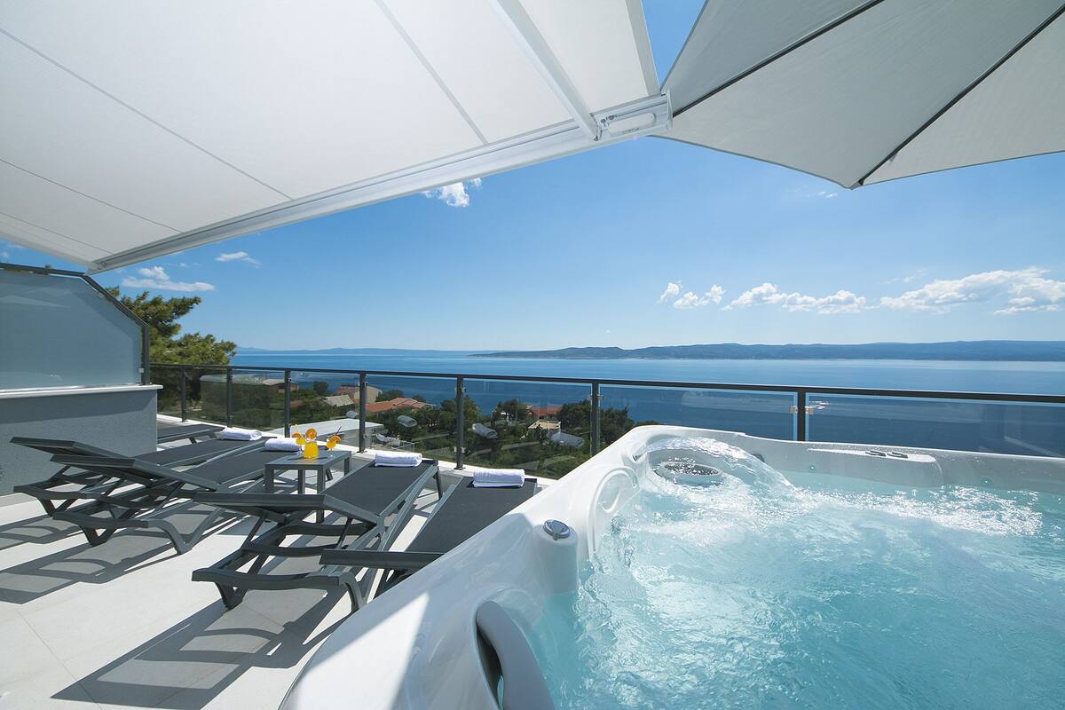 Une terrasse sur le toit dotée d’un jacuzzi et de chaises longues, offrant une vue sur une étendue d’eau.