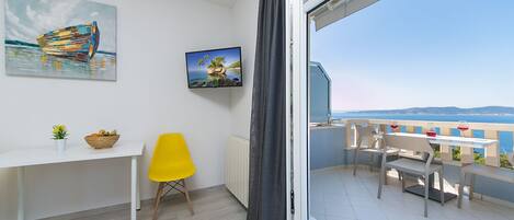 Un balcon avec une table et des chaises, une chaise jaune, un bureau blanc avec un panier, et deux tableaux accrochés au mur.