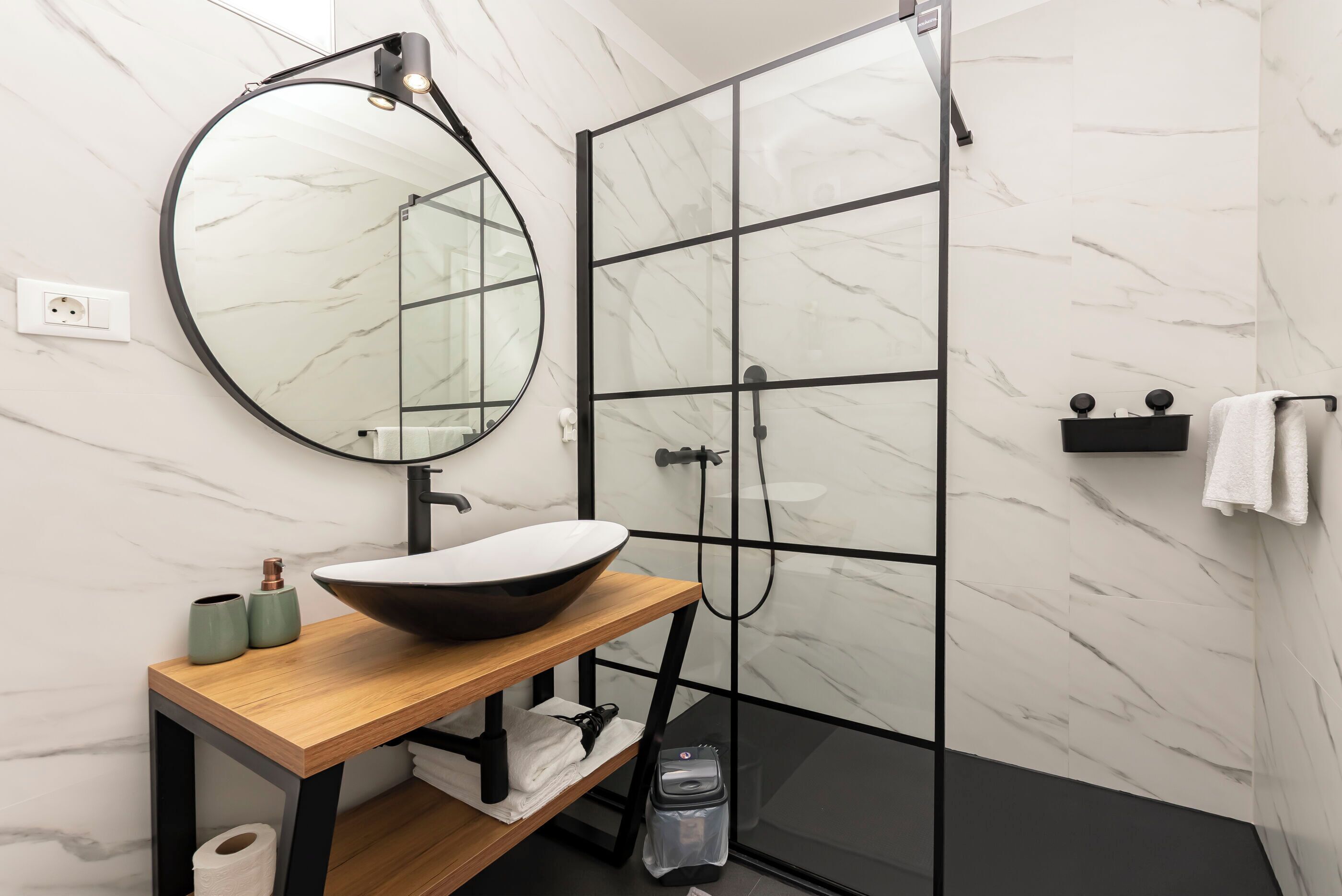 Een moderne badkamer met een houten wastafelmeubel, een ronde spiegel, een wastafel en een douchecabine met glazen wanden.