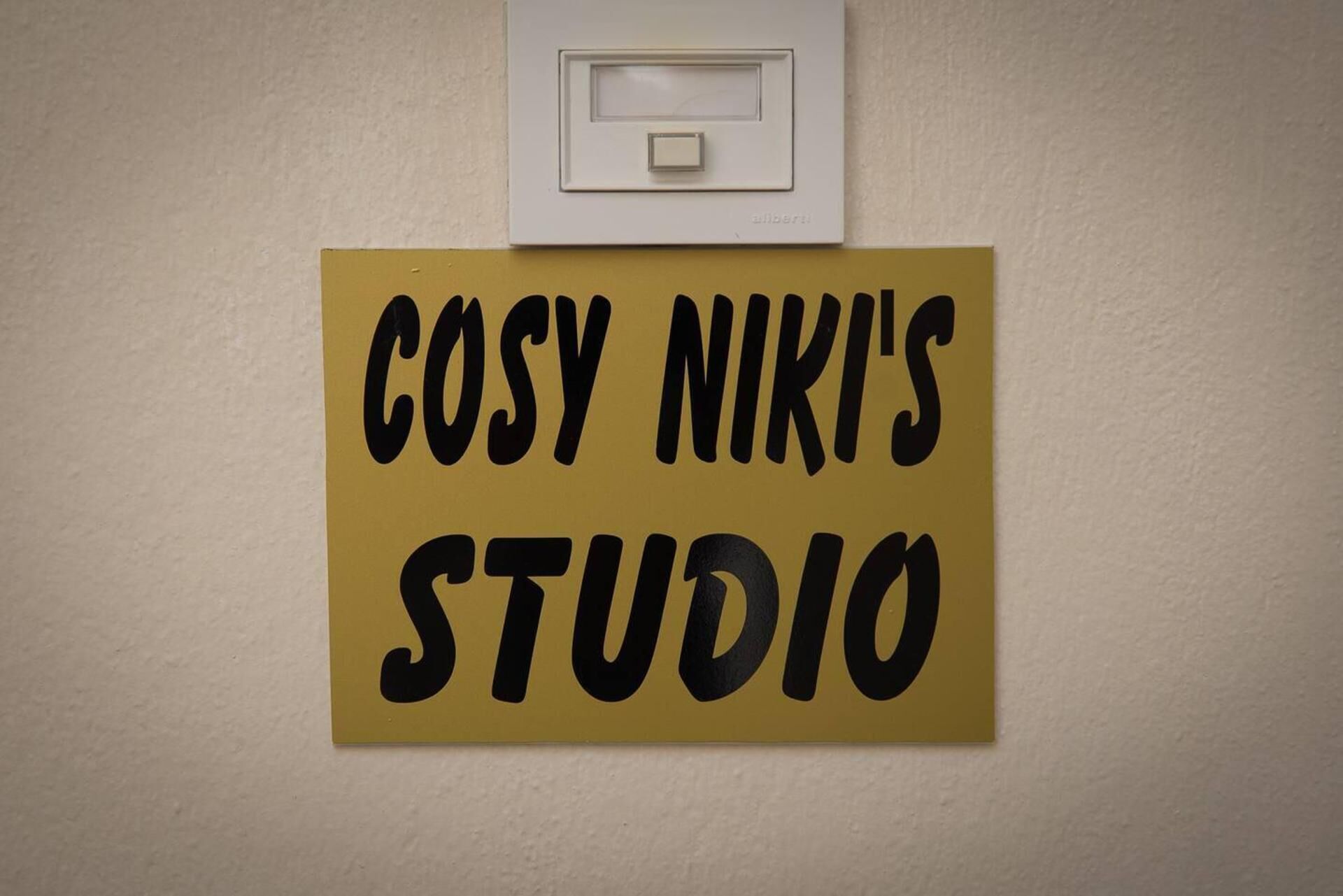 Ein Schild mit der Aufschrift 'COSY NIKI'S STUDIO' vor gelbem Hintergrund.