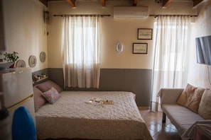 Um quarto com cama, mesa de cabeceira, cadeira e televisão.