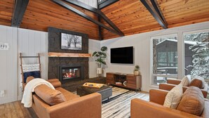 Un salon chaleureux avec une cheminée, des fauteuils confortables et une grande fenêtre donnant sur un paysage enneigé.