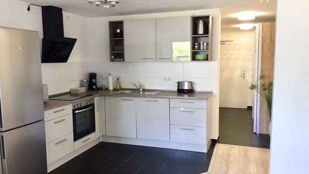 Una cocina moderna con armarios blancos, un refrigerador de acero inoxidable, horno integrado y piso de baldosas negras.