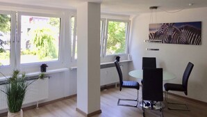Una sala de estar moderna con ventanas amplias, un comedor con una mesa redonda y sillas, y un cuadro de cebra en la pared.