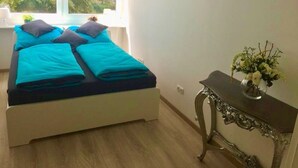 Un dormitorio con cama, almohadas, una mesita de noche y una ventana con persianas.