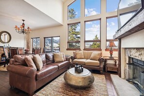 Relax in this cozy living space with a fireplace, leather sofa, and large windows offering a view of the outdoors.