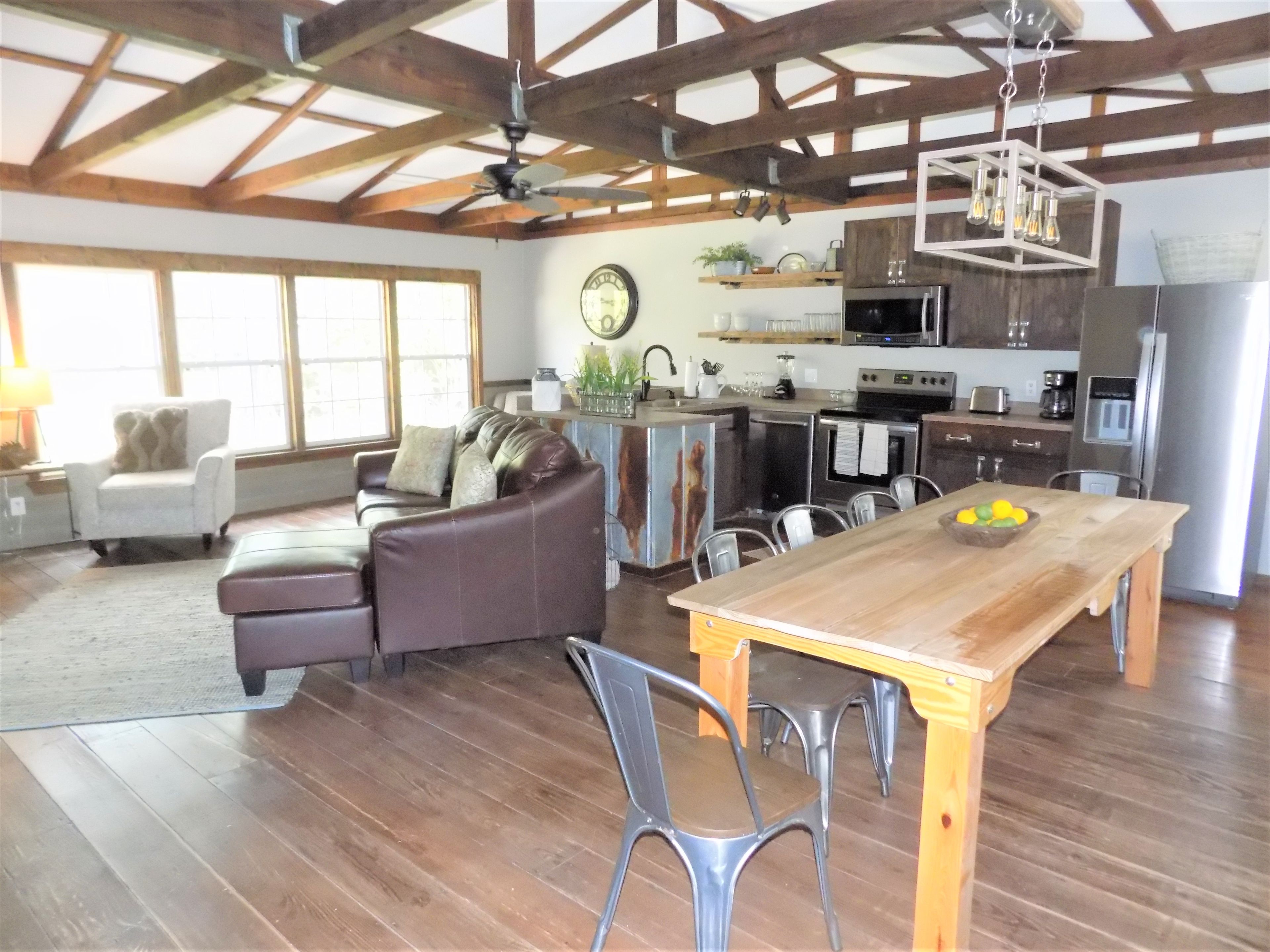 A spacious living area with a wooden dining table, a leather sofa, and a kitchen with modern appliances.