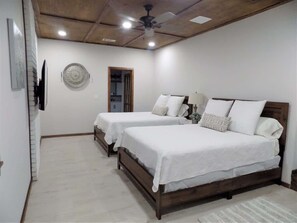 A bedroom with two beds, a ceiling fan, and a wall-mounted TV.