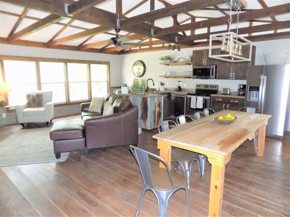 A spacious living area with a wooden dining table, a sofa, and a kitchen area with modern appliances.